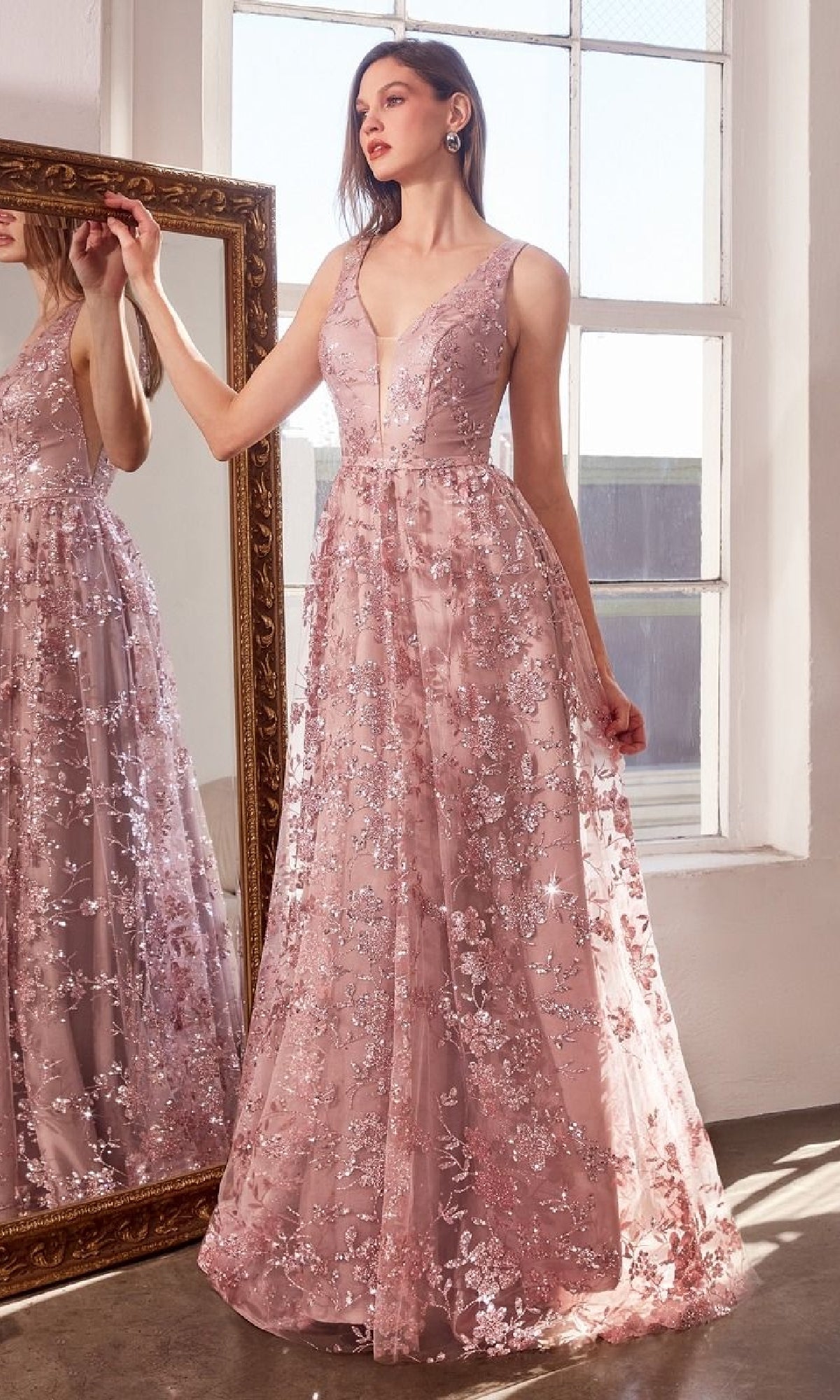 A woman stands in front of a mirror in a well-lit room, wearing the Amoris T606 Embroidered-Lace Long Prom Dress, featuring sleeveless pink lace with elegant floral embroidery.